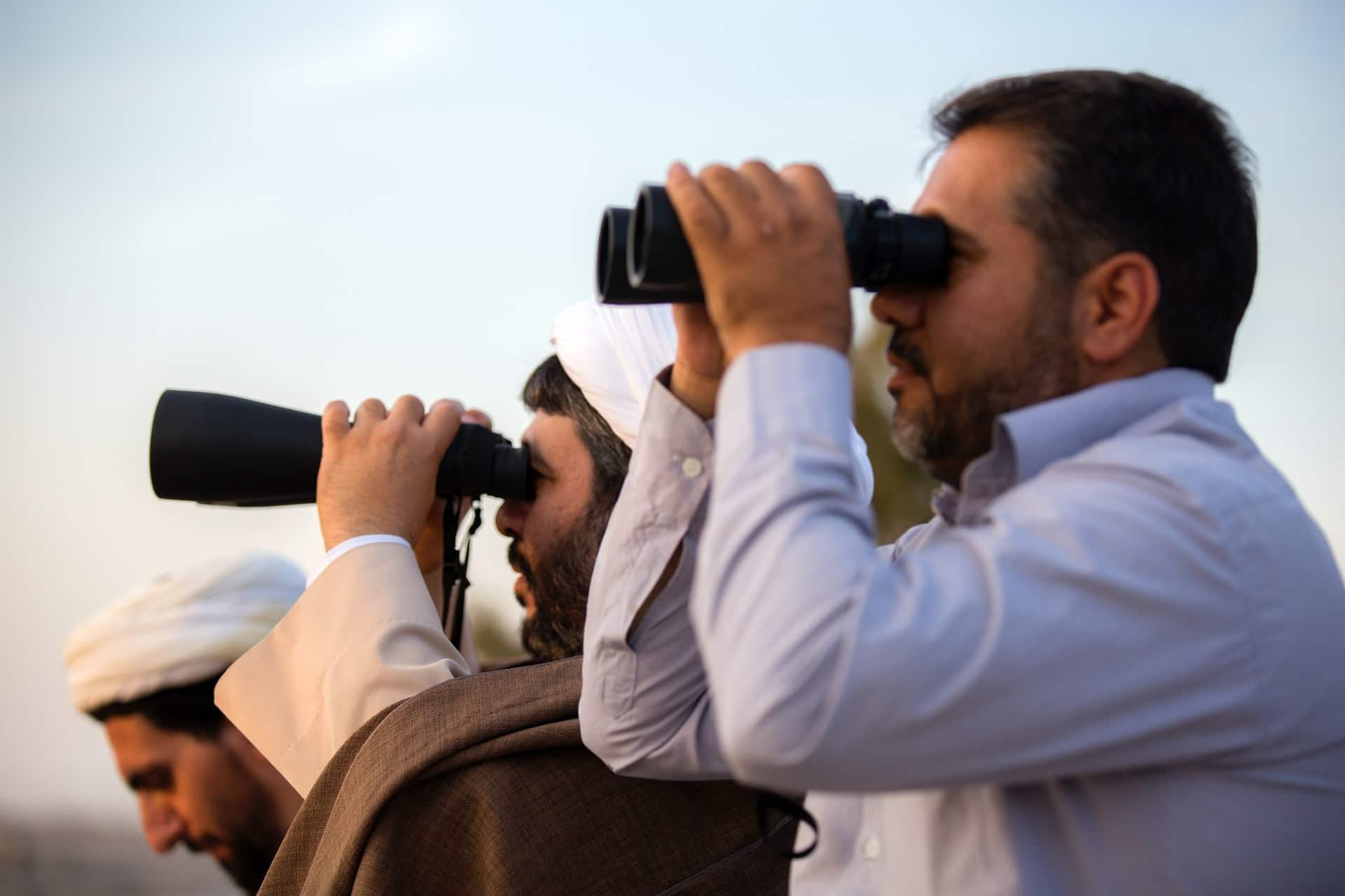 two men staring through binoculars while the third is looking down