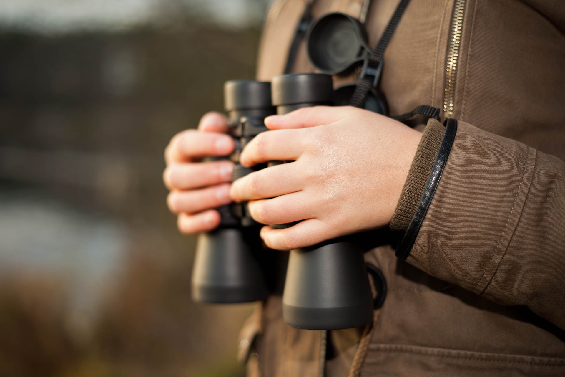 A person wearing a brown jacket holding black binoculars